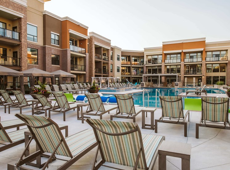 Rows of chaise lounge chairs around an outdoor pool surrounded by apartment buildings